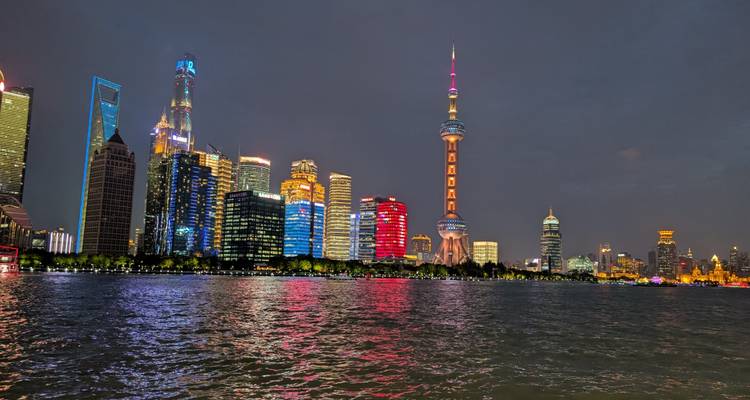 Vue nocturne de la skyline illuminée de Shanghai reflétant des couleurs vibrantes sur le fleuve Huangpu.