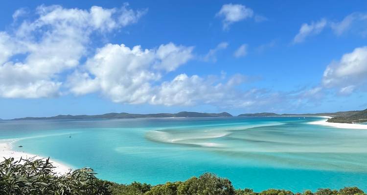 Vue panoramique sur la plage de Whitehaven avec des bancs de sable blanc tourbillonnants et une eau turquoise éclatante sous un ciel bleu