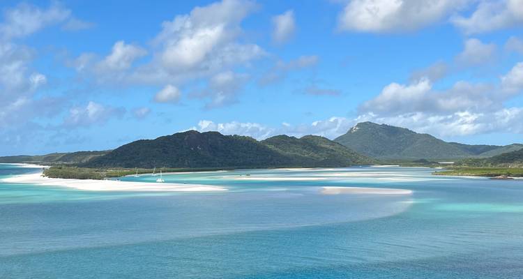 Les canaux turquoise et les vasières de sable blanc bordés par des îles vertes sous un ciel bleu éclatant