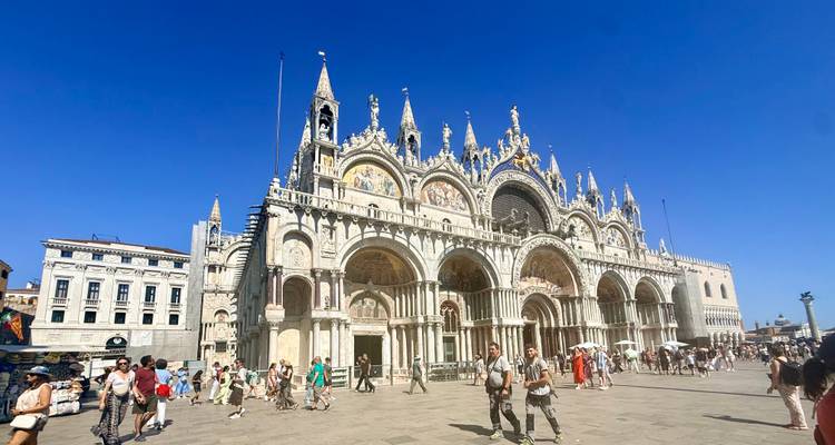 La Basílica de San Marcos domina la Piazza San Marco de Venecia bajo un cielo azul intenso con multitudes abajo.