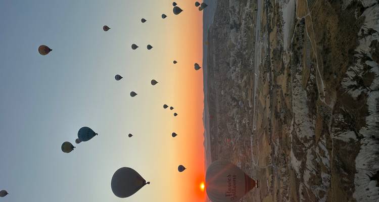 Des dizaines de montgolfières dérivent au-dessus des vallées façonnées de la Cappadoce tandis que le soleil se lève à l'horizon, peignant le ciel d'orange.