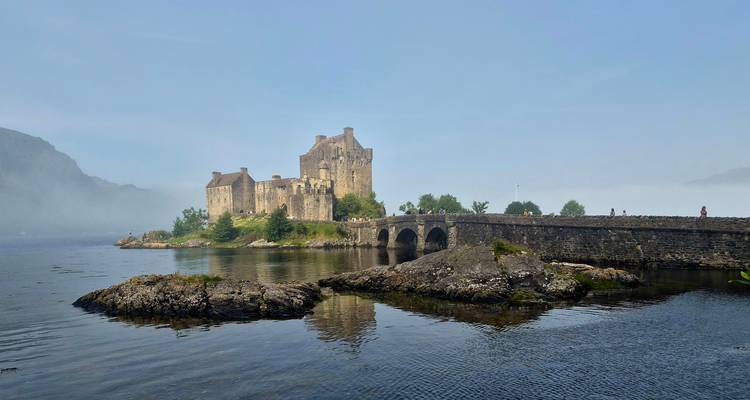Le château d'Eilean Donan s'élève de la brume au-dessus d'un pont de pierre et des eaux tidales réfléchissantes.