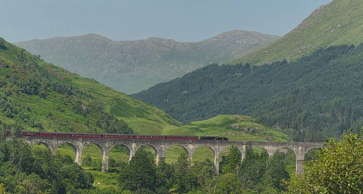 Le viaduc historique de Glenfinnan transporte un train à vapeur rouge à travers les paysages verdoyants des Highlands.