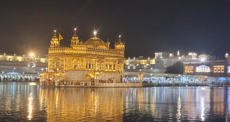 Templo Dorado iluminado de noche reflejándose en el tanque de agua tranquilo.