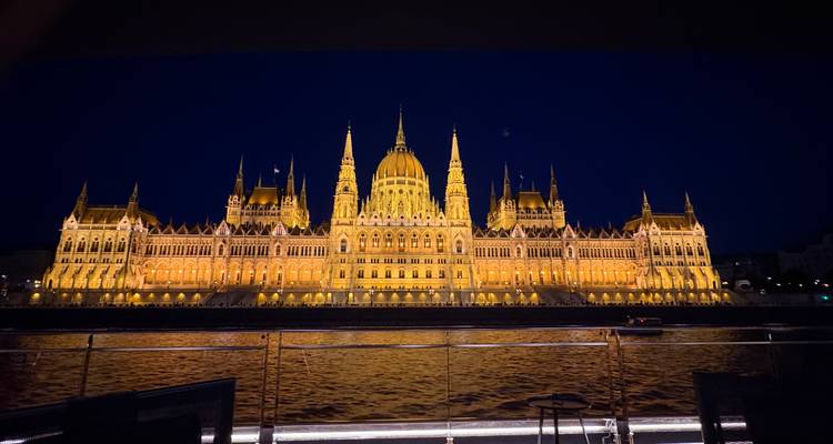 El Parlamento Húngaro iluminado brillando sobre el Río Danubio por la noche, visto desde la cubierta de un barco.