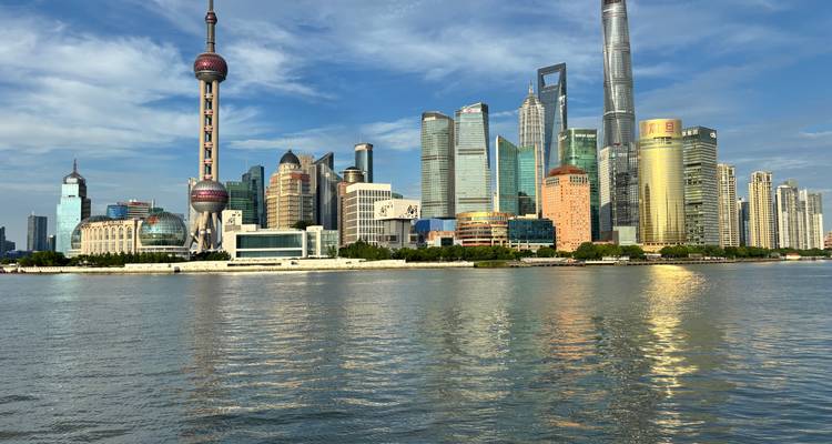 El icónico skyline de Shanghái con la Torre Oriental Pearl y rascacielos de cristal reflejados en el río Huangpu.