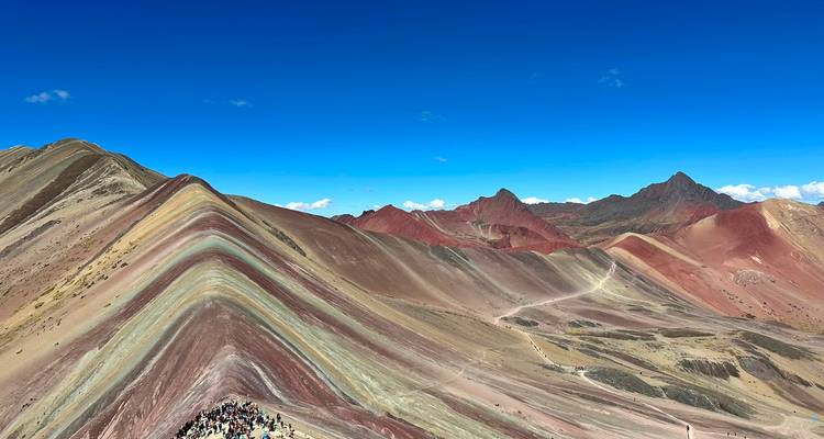 Vibrant striations of Rainbow Mountain undulate across a high Andean landscape under a brilliant blue sky.