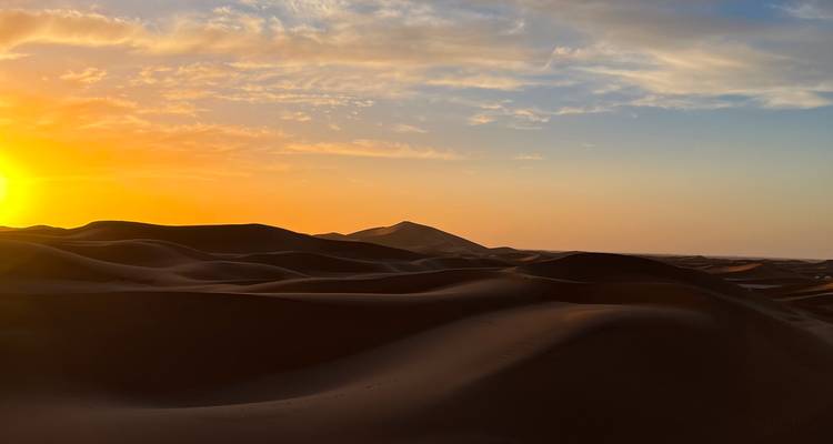 El atardecer dorado desciende sobre las dunas de arena que se extienden creando largas sombras en el desierto.