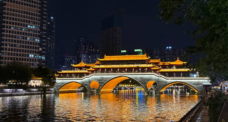 Puente Anshun iluminado reflejando luz dorada en el río Jin por la noche con el horizonte de la ciudad de fondo.