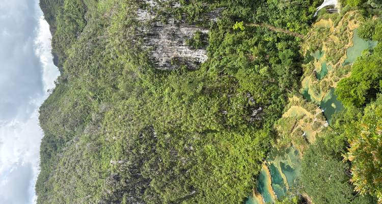 Des montagnes verdoyantes avec des bassins étagés turquoise et une rivière s'écoulant à travers une vallée de jungle profonde.