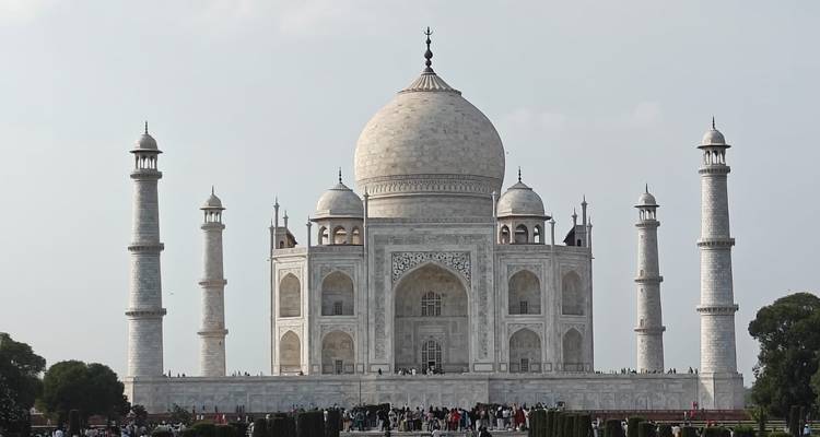 Vue de face du Taj Mahal avec ses quatre minarets et des foules de visiteurs à la base sous un ciel dégagé.