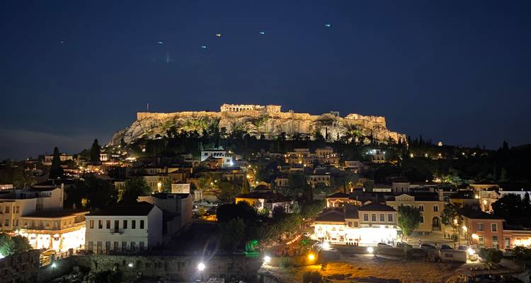 Panorámica nocturna de la colina de la Acrópolis iluminada sobre los tejados de Atenas
