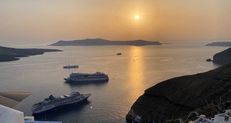Barcos de crucero anclados en la caldera de Santorini con el reflejo del sol dorado en el agua