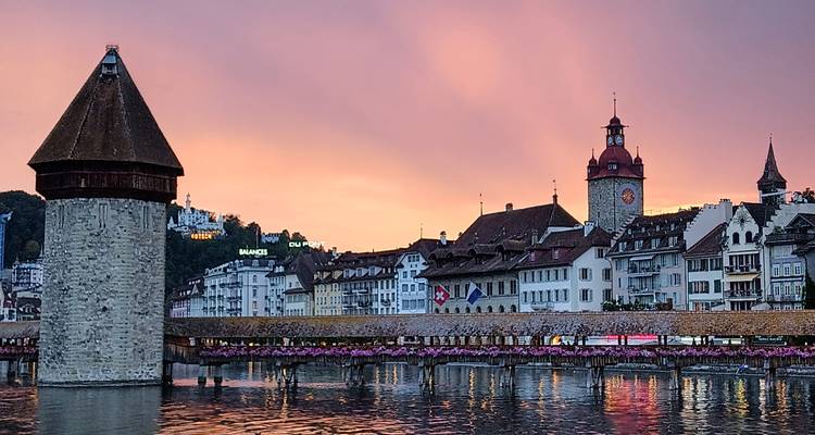 Chapel Bridge and Water Tower reflect in Lake Lucerne beneath a pink sunset sky.