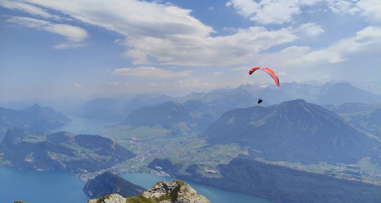 Paraglider soars high above deep blue lake and rugged alpine peaks.