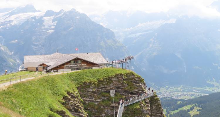 Clifftop restaurant and metal walkway overlook dramatic alpine valley and glaciers in Grindelwald.