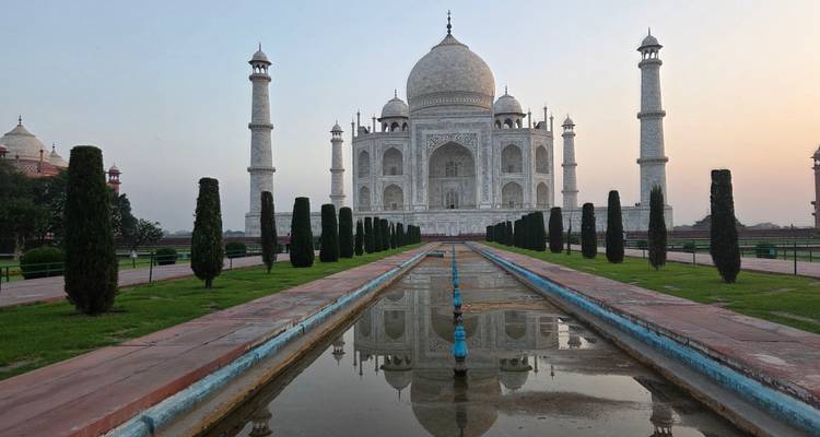 Vista simétrica del Taj Mahal al amanecer reflejada en un largo canal de agua.