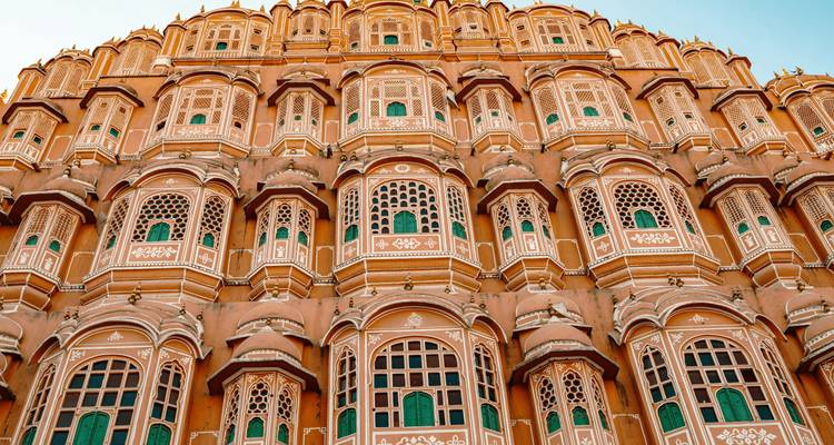 Façade symétrique du Hawa Mahal de Jaipur avec des rangées de fenêtres à treillis illuminées par une lumière chaude.