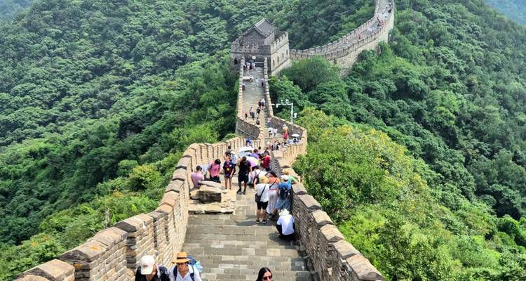 Busy section of the Great Wall of China snaking across green mountains filled with tourists.
