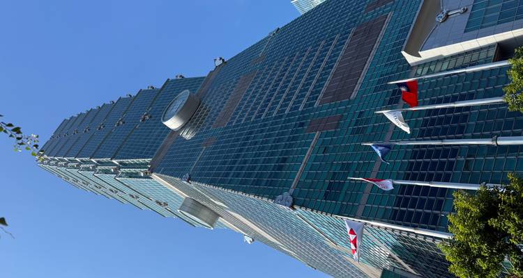 Toma dramática de ángulo bajo del rascacielos Taipei 101 bajo un cielo azul despejado con banderas