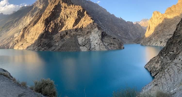 Un lac d'un turquoise éclatant est entouré de parois rocheuses abruptes et ensoleillées ainsi que de pics montagneux majestueux.