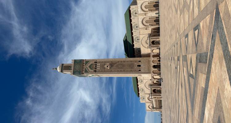 Weitläufiger Blick auf das aufragende Minarett und den großen Platz der Hassan-II.-Moschee unter dramatischen Wolken.
