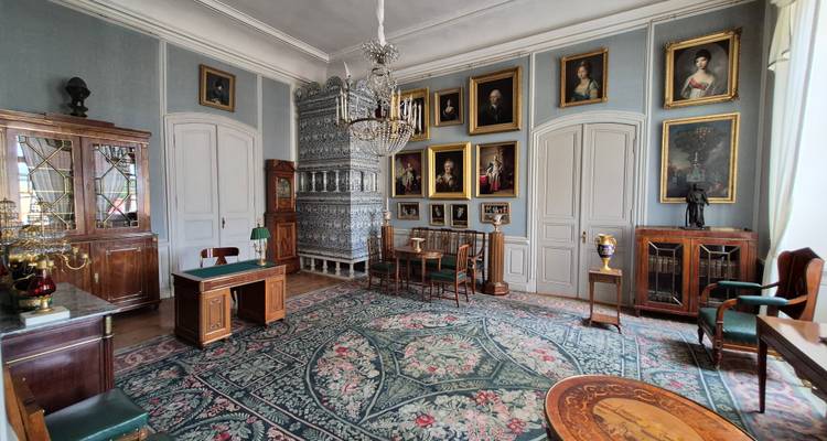 Salle d'étude de période somptueuse avec mobilier ancien, tapis à tapisserie, portraits et radiateur en céramique orné.