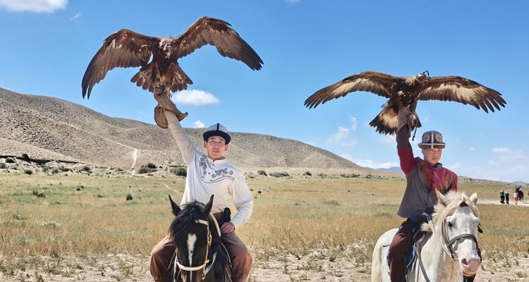 Deux cavaliers en tenue traditionnelle élèvent des aigles dorés vers le ciel sur une steppe ouverte sous des ciels bleus.
