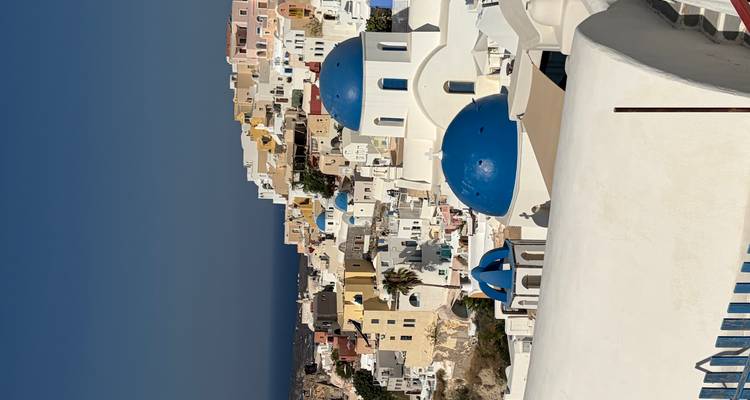 Classic view of white Cycladic houses and blue domes cascading down a cliff in Santorini.