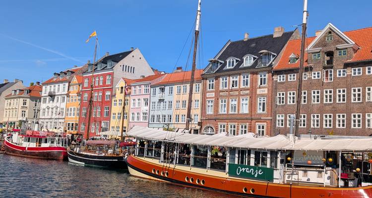 Des maisons colorées du dix-septième siècle bordent un waterfront animé avec des bateaux classiques sous un soleil éclatant.