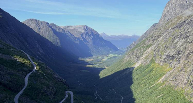 Spektakuläre Talaussicht von einer hohen Serpentinenstraße in den Bergen mit tiefen Schatten und entferntem Ackerland in Norwegen.