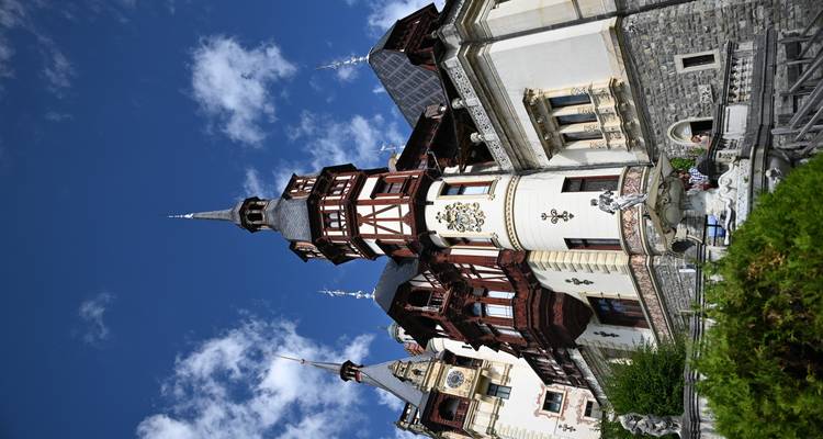 Le château ornemental de Peleș avec ses tours à colombages et sa façade en pierre se dressant contre un ciel bleu brillant.