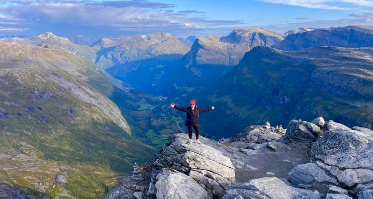 Le voyageur se tient triomphalement au sommet rocheux avec des vues panoramiques sur les vallées profondes et les pics.