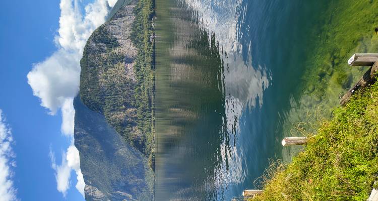Lago cristalino reflejando montañas verdes y un cielo azul con nubes dispersas en Hallstatt.
