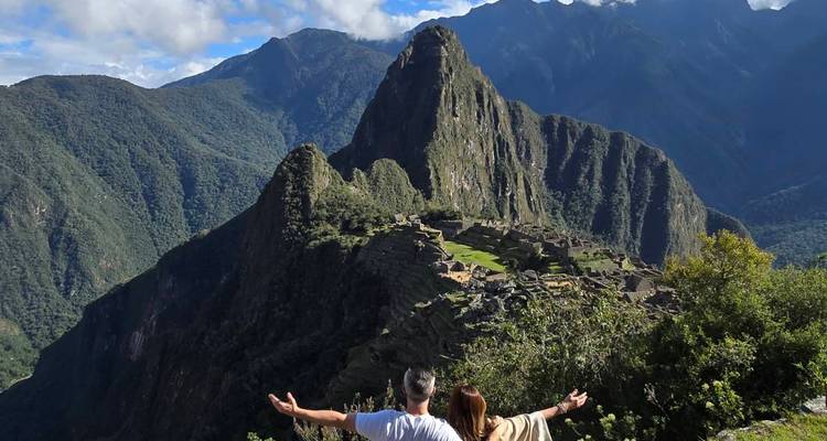Pareja con los brazos extendidos admirando las icónicas terrazas y el pico de Machu Picchu desde un punto de vista elevado