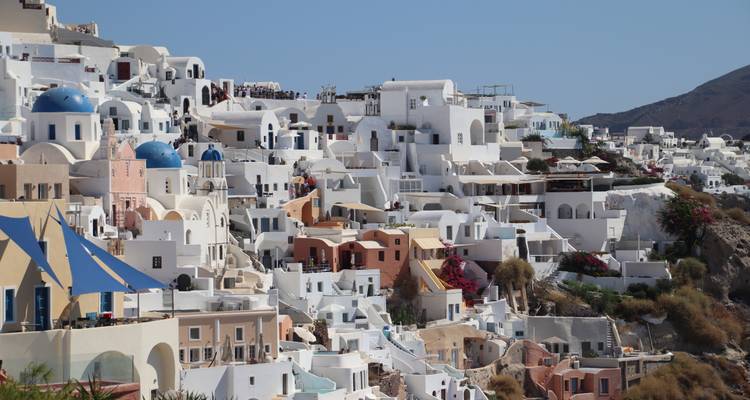 Les maisons blanchies à la chaux emblématiques et les églises aux dômes bleus regroupées sur les falaises d'Oia, Santorin, sous un ciel dégagé.