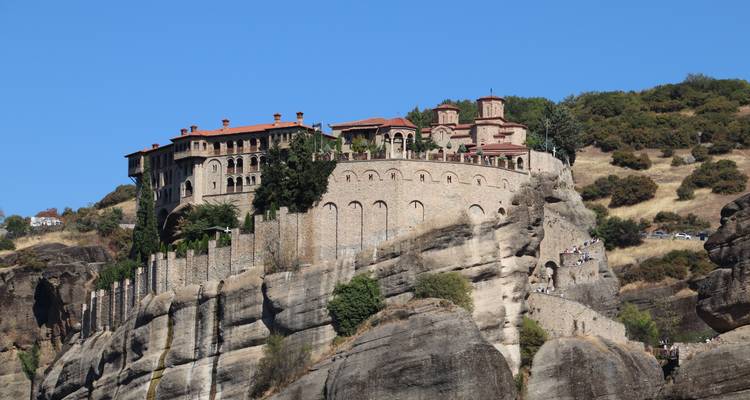 Monastère perché au sommet de falaises de grès imposantes à Meteora sous un ciel bleu clair.
