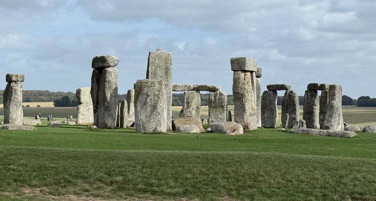 Icónico círculo de piedra de Stonehenge bajo un cielo parcialmente nublado con campos más allá.