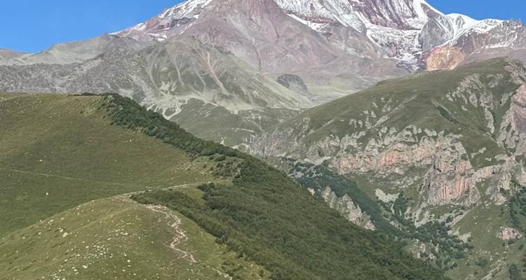 Snow-capped Mount Kazbek rising above rolling green ridges under a clear blue sky.