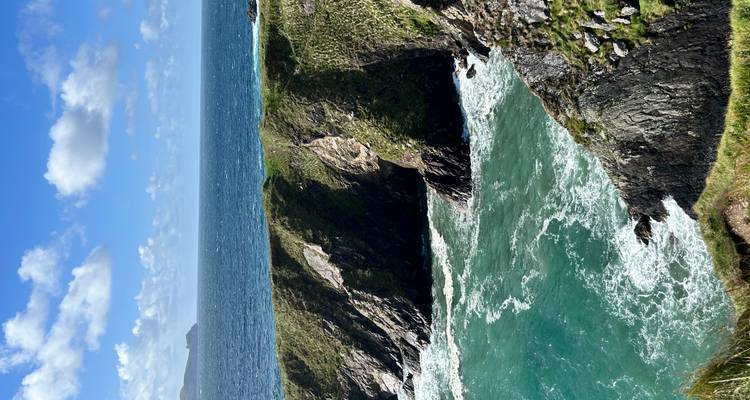 Dramatische zeeën kliffen en turquoise Atlantische wateren met golven die onder een groen uitstekend stuk land tegen de rotsen beuken