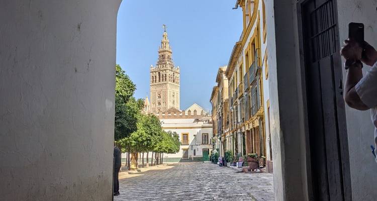 Uitzicht door een witte boog naar Sevilla's Giralda-klokkentoren die boven een rustige keistenen straat uittorent met historische gebouwen aan beide zijden.