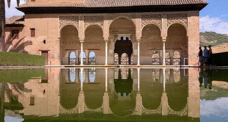 Elegante Moorse bogen van het Alhambra die zich perfect spiegelen in een rustig groen zwembad op een zonnige dag.