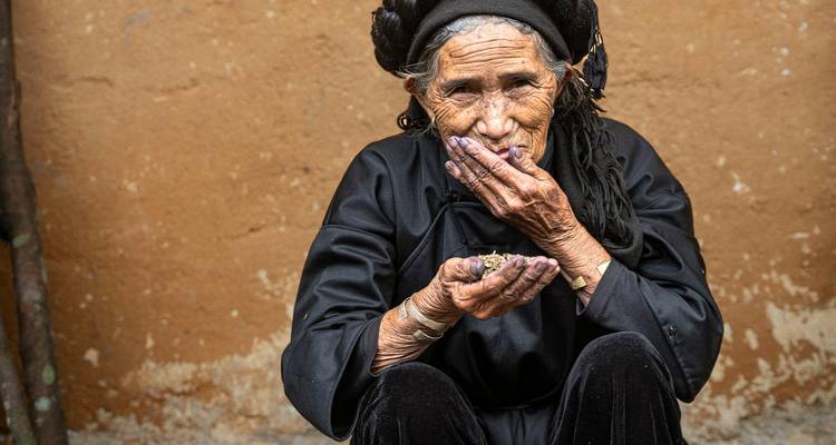 Portrait d'une femme âgée vêtue d'une tenue traditionnelle noire tenant pensivement des haricots secs.