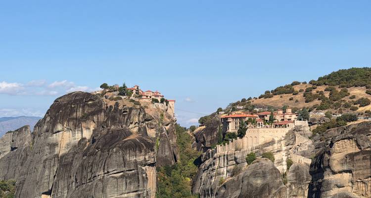 Des monastères spectaculaires perchés au sommet de piliers rocheux imposants sous un ciel bleu dégagé.