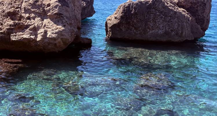 Eau de mer turquoise cristalline scintillant autour de grandes roches côtières.