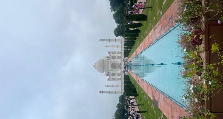 Vue classique symétrique du Taj Mahal avec bassin de réflexion et jardins taillés sous un ciel voilé.