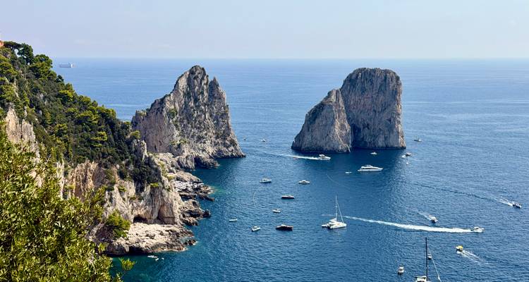 Les bateaux naviguent autour des spectaculaires formations rocheuses des Faraglioni au large de la côte accidentée de Capri.