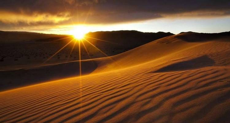 Amanecer sobre dunas de desierto onduladas que proyectan largas sombras y un dramático destello de estrella