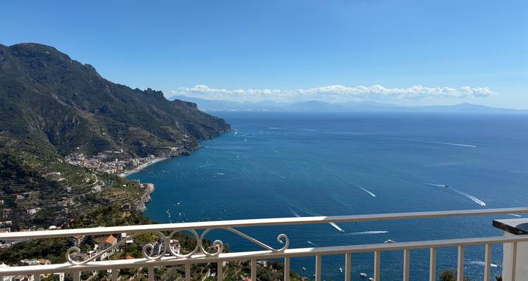 Vue panoramique spectaculaire des falaises de la Côte Amalfitaine et de la mer bleu profond depuis une balustrade de balcon.