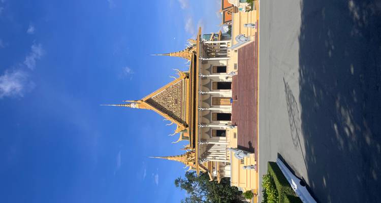Groot gouden Khmer-paleis met sierlijke torens staat onder een strakblauwe hemel, omgeven door een brede stenen binnenplaats.